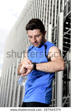young sport man checking time on chrono timer runners watch holding water bottle after training session in business district with urban office building background in fitness concept