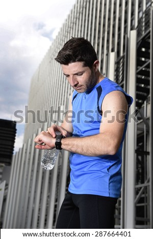 young sport man checking time on chrono timer runners watch holding water bottle after training session in business district with urban office building background in fitness concept