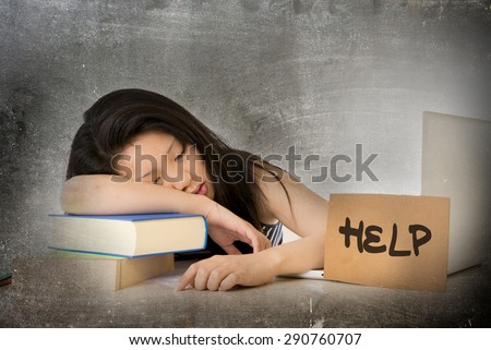young pretty Asian Chinese woman student asleep on her laptop studying overworked with help sign leaning tired and overwhelmed on textbooks in stress eduction concept in grunge dirty background