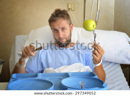 young man in hospital room after suffering accident eating healthy apple as  diet clinic food in moody and sad face expression disliking the medical center meal