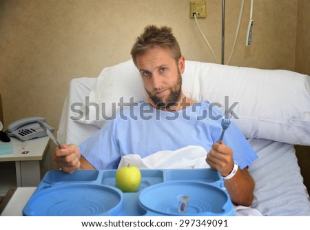 young man in hospital room after suffering accident eating healthy apple as  diet clinic food in moody and sad face expression disliking the medical center meal