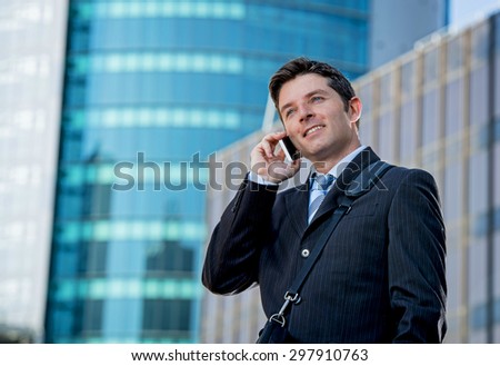 young attractive businessman in suit and necktie talking on mobile smart phone smiling happy and confident standing outdoors in exterior office buildings on business district in success concept