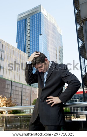 young exhausted and worried businessman standing outdoors on street in front of business buildings at financial district looking desperate and sad in work stress and depression concept