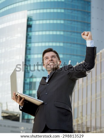 young attractive and successful businessman in suit and tie with computer laptop happy and excited doing victory sign after reaching business goal outdoors in financial district
