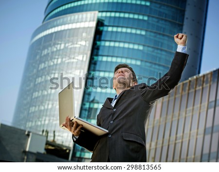 young attractive and successful businessman in suit and tie with computer laptop happy and excited doing victory sign after reaching business goal outdoors on financial district street