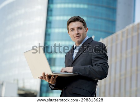 young attractive businessman in suit and necktie holding computer laptop happy and relaxed standing outdoors at financial district in business success concept