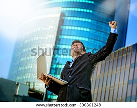 young attractive and successful businessman in suit and tie with computer laptop happy and excited doing victory sign celebrating success outdoor on financial district street