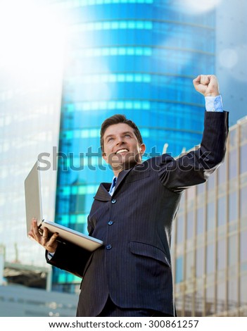 young attractive and successful businessman in suit and tie with computer laptop happy and excited doing victory sign celebrating success outdoor on financial district street