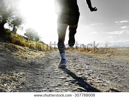close up silhouette legs and feet of extreme cross country man running training on rural track jogging at sunset with harsh sunlight and lens flare in countryside sport and healthy lifestyle concept