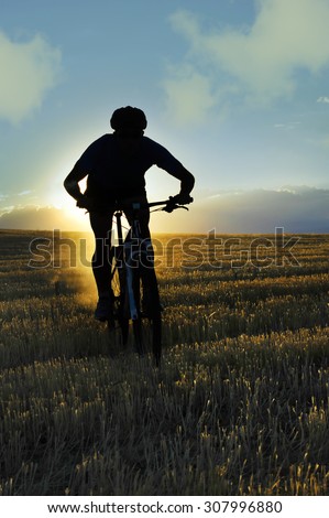 silhouette of sport man cycling downhill riding cross country mountain bike on sunset field with harsh sun light and high contrast in amazing beautiful rural landscape