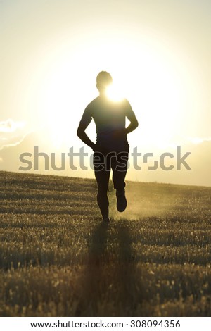 silhouette of young sport man running off road in countryside straw field with strong backlight at summer sunset in a beautiful rural landscape in healthy lifestyle and training concept