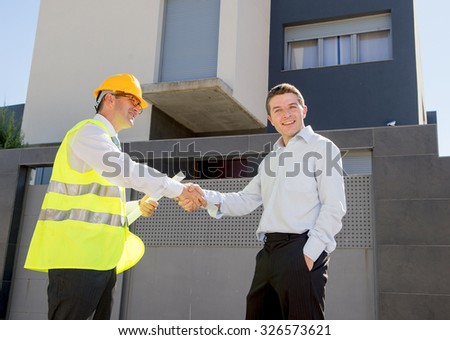 happy customer smiling and constructor foreman worker with helmet and vest holding blueprints handshake agreement in real state business and housing industry concept