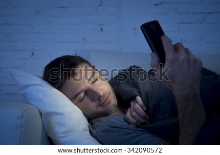 young man in bed couch at home falling asleep late at night while using mobile phone in low light relaxed in communication technology addiction and internet social network concept