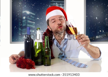 drunk happy business man in Santa hat with alcohol bottles in new year toast with champagne glass smiling drinking too much at Christmas party at night in the office