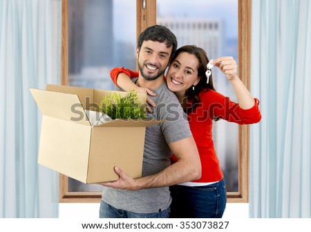 young happy Hispanic couple moving together in a new flat or apartment carrying cardboard boxes home belongings holding house key smiling in housing and real state concept