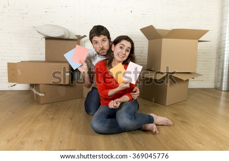 young happy married couple sitting on flat floor unpacking cardboard boxes moving in new home apartment smiling happy with color chart planning for decoration of the house in real estate concept