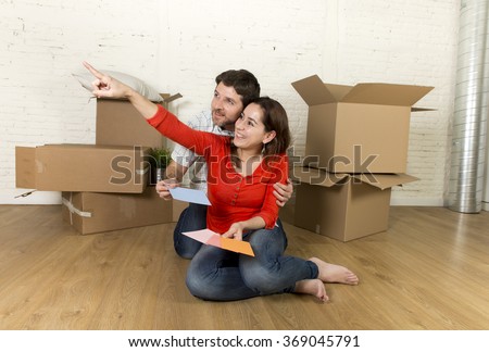 young happy married couple sitting on flat floor unpacking cardboard boxes moving in new home apartment smiling happy with color chart planning for decoration of the house in real estate concept