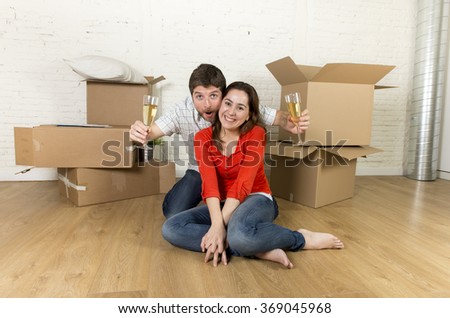young happy married couple sitting on flat floor unpacking cardboard boxes celebrating with champagne toast moving in new home apartment smiling happy in real estate concept