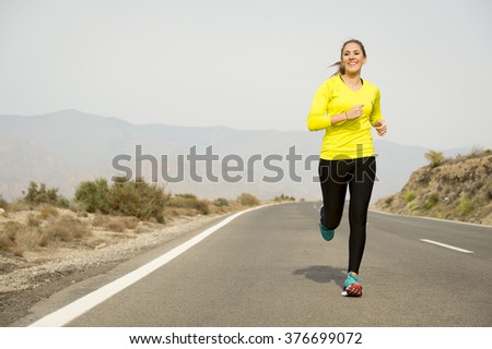 young attractive sport woman running on asphalt road with desert mountain landscape background looking happy and healthy in jogging training workout , fitness and wellness concept