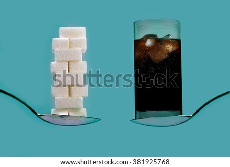 spoon with stack of sugar cubes piled  compared with cola refresh drink in sweet excess calories content,  diet and glucose addiction concept isolated on blue background