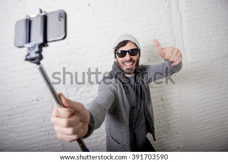 young attractive man in casual clothes beanie hipster style holding selfie stick mobile phone shooting self portrait photo or recording video in internet blog and blogger concept