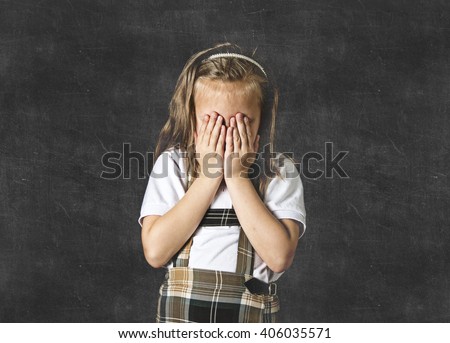 young sweet junior schoolgirl with blonde hair crying sad and shy standing isolated in front of school class blackboard wearing school uniform in children education stress and bullying victim