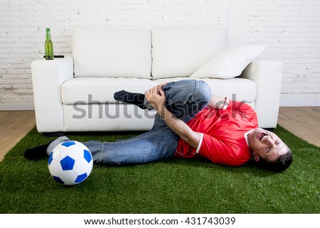 fanatic football fan lying on green grass carpet emulating soccer stadium pitch mocking player in pain hurt on ankle while watching game on television in crazy supporter parody concept