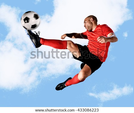 young football player kick ball in skillful volley jumping on the air in dynamic pose wearing red jersey and socks isolated on blue sky background shot in sport advertising style