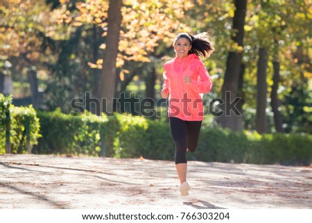 young attractive and happy runner woman in Autumn sportswear running and training on jogging outdoors workout in city park with trees and yellow leaves in fitness and healthy lifestyle concept