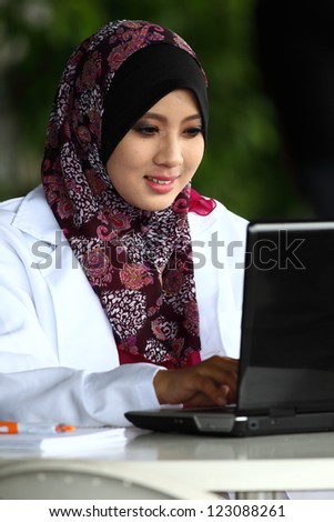 A young muslim girl doctor with hijab (head scarf) typing something on the laptop