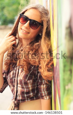 Beautiful girl stands near the wall with graffiti on a warm sunny day. fashion portrait