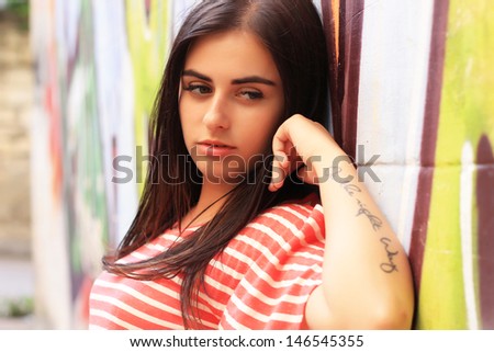 Beautiful brunette girl stands near the wall with graffiti on a warm sunny day. fashion portrait