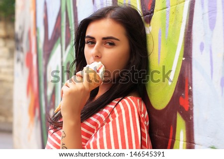 Beautiful brunette girl stands near the wall with graffiti on a warm sunny day. fashion portrait