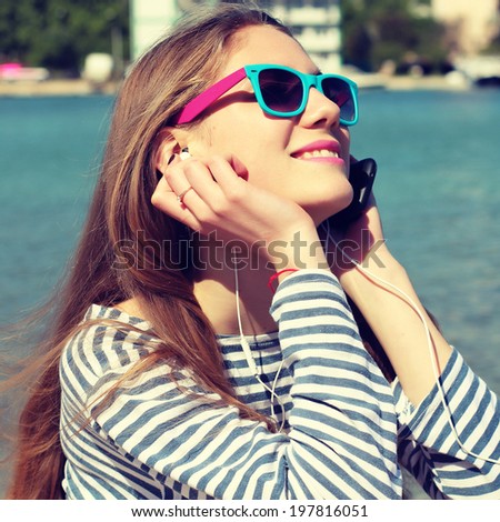Portrait of a funny young girl on beach listening to music in earphones from smart phone mp3 player. Photo toned style Instagram filters