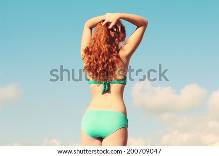 Girl with a beautiful figure stands with his back to the camera. Sexy red haired girl in a swimsuit. Photo toned style instagram filters