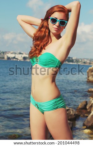 Outdoor fashion portrait of beautiful red-haired sexy woman with perfect athletic body enjoy your holiday. Wearing bright stylish bikini and sunglasses. Photo toned style instagram filters