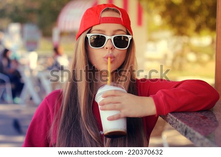 Outdoor closeup portrait of pretty stylish fashion girl having fun drinking chocolate milkshake in a cafe outdoors.  Lifestyle swag style photo with a vintage retro instagram filter