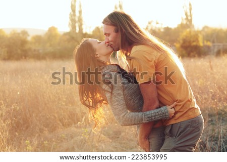 Sensual outdoor portrait of young stylish fashion couple kissing in autumn field. Photo toned style Instagram filters.