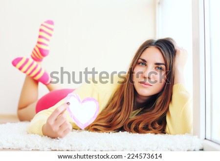Beautiful young woman in colorful cloths lying on floor and holding valentines heart with a retro vintage instagram filter.
