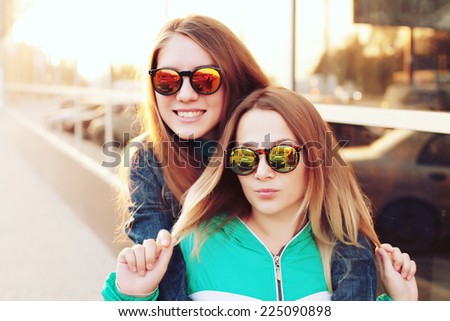 Close up fashion portrait of two young hipster girl friends, wearing mirrored sunglasses, having blonde and ombre hairs. Outdoors, lifestyle trendy photography with a retro vintage instagram filter.