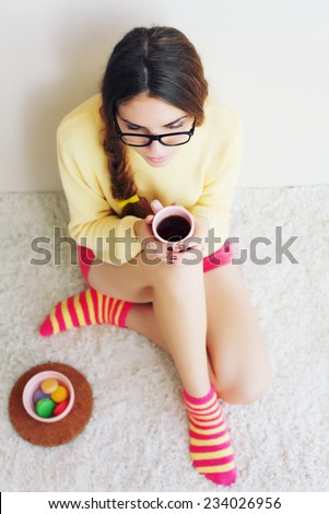Beautiful funny young girl in bright socks and shorts sitting on a white carpet is reading a book and eating French macaroon.