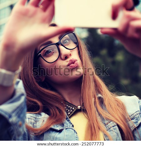Pretty young female tourist makes selfie. Beautiful urban woman taking picture of herself. Filtered image.