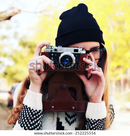 Outdoor lifestyle portrait of pretty young woman having fun with camera travel photo of photographer. Making pictures in hipster style glasses and hat