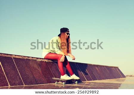 Outdoor closeup summer portrait of pretty girl posing in urban youth style. Fashion lifestyle. Beautiful young woman having fun together with skate board. Photo toned style instagram filters