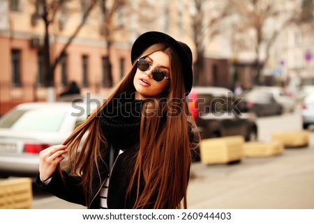 Outdoor fashion image of stylish beautiful brunette young woman wearing scarf, sunglasses and vintage hat, walking on the street.