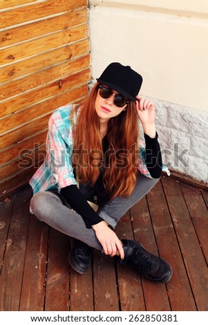 Portrait of beautiful cool young woman gesturing in hat and sunglasses over grunge wall. Swag girl. Sexy fashion portrait toned style Instagram filters.