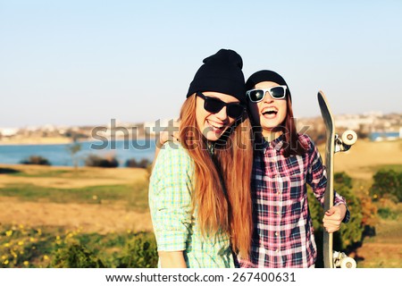 Two teen girl friends having fun together with skate board. Outdoors, urban lifestyle. Photo toned style Instagram filters.