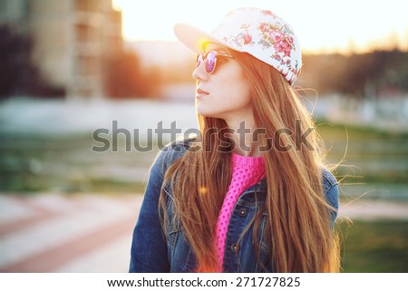 Outdoor fashion portrait of stylish swag girl, wearing swag cap, trendy sunglasses and denim jacket, amazing view of the beach at sunset. Lifestyle picture toned with a vintage instagram filter effect
