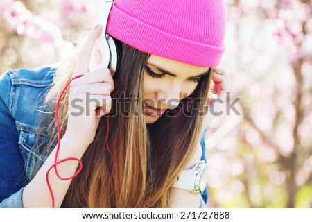 Close up portrait of a funny young swag girl on lush garden listening to music in earphones from smart phone mp3 player. Outdoors, lifestyle. Photo toned style Instagram filters