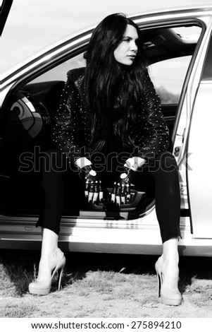 Black and white fashion outdoor photo of beautiful sexy girl with long brunette hair in leather jacket, car driver woman